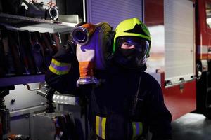 detiene tubo flessibile. maschio pompiere nel protettivo uniforme in piedi vicino camion foto