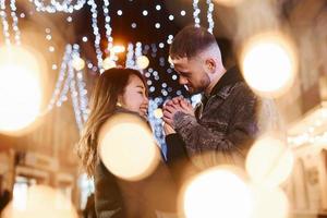 artificiale illuminazione di ghirlande. contento multirazziale coppia insieme all'aperto nel il città festeggiare nuovo anno foto