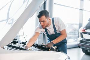 qualità servizio. giovane uomo nel bianca camicia e blu uniforme riparazione automobile foto