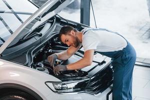 cappuccio è ha aperto. giovane uomo nel bianca camicia e blu uniforme riparazione automobile foto