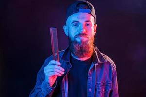giovane barbuto barbiere nel berretto in piedi nel il studio con neon illuminazione foto