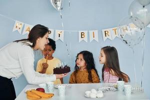 donna detiene torta. bambini su festeggiare compleanno festa in casa avere divertimento insieme foto