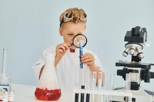 assunzione un' vicino Guarda a liquido nel test tubo. bambini nel bianca cappotti giochi un' scienziati nel laboratorio di utilizzando attrezzatura foto