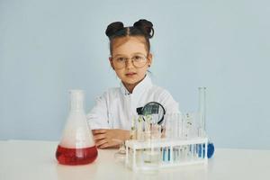 poco ragazza nel cappotto giocando un' scienziato nel laboratorio di utilizzando attrezzatura foto