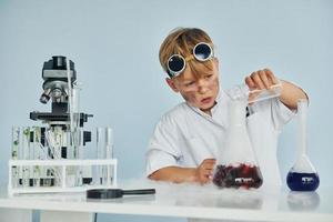 poco ragazzo nel cappotto giocando un' scienziato nel laboratorio di utilizzando attrezzatura foto