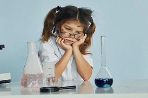 senza esito sperimentare. poco ragazza nel cappotto giocando un' scienziato nel laboratorio di utilizzando attrezzatura foto