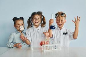 contento amici sorridente. bambini nel bianca cappotti giochi un' scienziati nel laboratorio di utilizzando attrezzatura foto