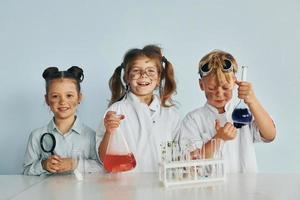 contento amici sorridente. bambini nel bianca cappotti giochi un' scienziati nel laboratorio di utilizzando attrezzatura foto