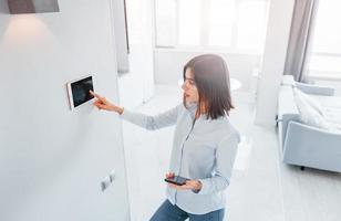 usi tavoletta quello è montato nel il parete. giovane donna è in casa nel inteligente Casa camera a giorno foto