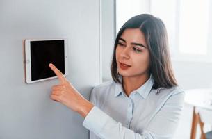 usi tavoletta quello è montato nel il parete. giovane donna è in casa nel inteligente Casa camera a giorno foto