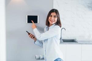 controllo Casa di uno tocco. giovane donna è in casa nel inteligente Casa camera a giorno foto