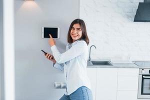 controllo Casa di uno tocco. giovane donna è in casa nel inteligente Casa camera a giorno foto