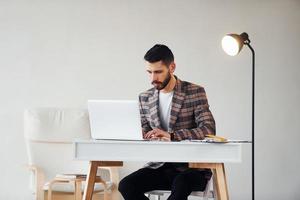 usi il computer portatile. giovane elegante uomo d'affari nel completo da uomo al chiuso. concezione di successo foto