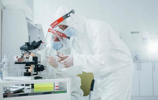 utilizzando microscopio. femmina medico lavoratori nel protettivo uniforme lavori su covid-19 vaccino foto