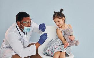 giovane africano americano medico dando iniezione per poco ragazza a ospedale foto