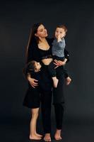 donna nel nero elegante Abiti è con sua poco figlio e figlia nel il studio foto