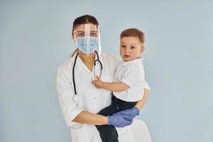 giovane infermiera nel bianca cappotto e con stetoscopio detiene poco ragazzo nel mani foto