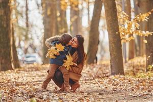 giocando con le foglie. madre con sua figlio è avendo divertimento all'aperto nel il autunno foresta foto