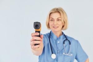 con infrarosso termometro. di mezza età professionale femmina medico nel uniforme e con stetoscopio foto