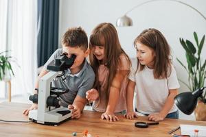 utilizzando microscopio. bambini avendo divertimento nel il domestico camera a giorno insieme foto
