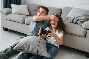 giocando videogiochi. bambini avendo divertimento nel il domestico camera a giorno insieme foto