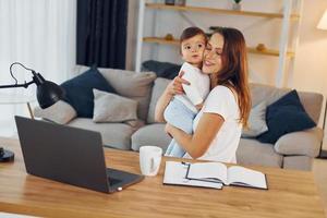 il computer portatile è su il tavolo. madre con sua poco figlia è a casa insieme foto