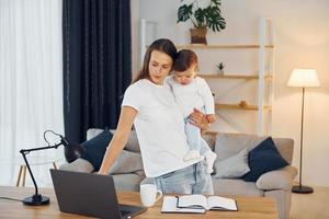 utilizzando il computer portatile. madre con sua poco figlia è a casa insieme foto