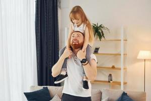 ragazza seduta su il le spalle. padre con il suo poco figlia è a casa insieme foto