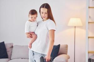 donna usi vuoto più pulito. madre con sua poco figlia è in casa a casa insieme foto