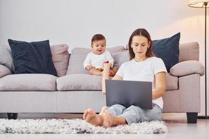 donna Lavorando di utilizzando il computer portatile. madre con sua poco figlia è in casa a casa insieme foto