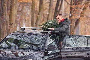 nel il foresta. uomo con poco verde abete è all'aperto vicino il suo macchina. concezione di vacanze foto