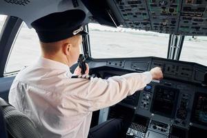 pilota nel formale indossare si siede nel il cabina di pilotaggio e controlli aereo foto