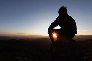 silhouette di un' giovane uomo preghiere per Dio su il montagna a tramonto sfondo. donna raccolta il suo mani nel culto. cristiano religione concetto. foto