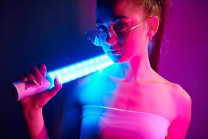 con illuminazione attrezzatura. alla moda giovane donna in piedi nel il studio con neon foto