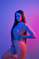Spettacoli corpo. alla moda giovane donna in piedi nel il studio con neon leggero foto