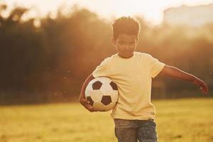 giovane calcio giocatore. africano americano ragazzo avere divertimento nel il campo a estate giorno foto