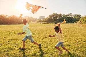 in esecuzione con aquilone. Due africano americano bambini avere divertimento nel il campo a estate giorno insieme foto