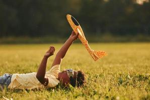 posa giù con giocattolo aereo su il erba. africano americano ragazzo avere divertimento nel il campo a estate giorno foto