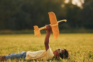 posa giù con giocattolo aereo su il erba. africano americano ragazzo avere divertimento nel il campo a estate giorno foto