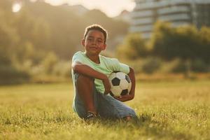 assunzione un' rompere. con calcio sfera. africano americano ragazzo avere divertimento nel il campo a estate giorno foto