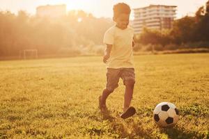 giochi calcio. africano americano ragazzo avere divertimento nel il campo a estate giorno foto