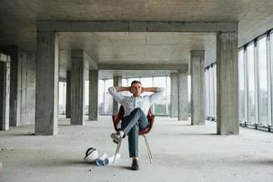 si siede su il sedia. giovane uomo nel formale indossare è Lavorando in casa su il costruzione foto