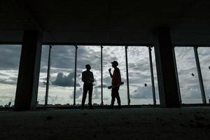 in piedi contro grande finestra. uomo nel completo da uomo e tuttofare nel arancia protettivo indossare è Lavorando su costruzione foto