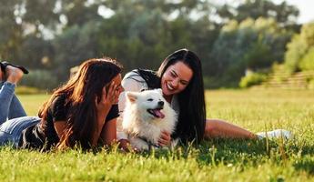 Due donne avendo un' riposo mentre posa giù su il terra di campo con loro carino cane foto