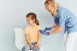 poco ragazza nel giallo camicia. medico nel uniforme fabbricazione vaccinazione per il paziente foto