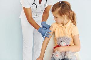 carino poco ragazza. medico nel uniforme fabbricazione vaccinazione per il paziente foto