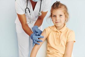 carino poco ragazza. medico nel uniforme fabbricazione vaccinazione per il paziente foto