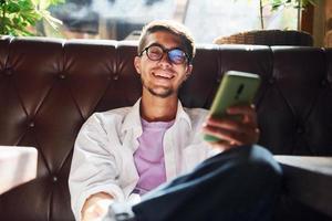 con Telefono nel mano. uomo nel casuale Abiti seduta nel il pub foto