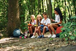 seduta e avendo un' riposo. bambini passeggiando nel il foresta con viaggio attrezzatura foto