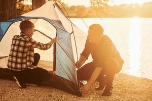 padre e figlio installazione tenda all'aperto vicino il lago foto